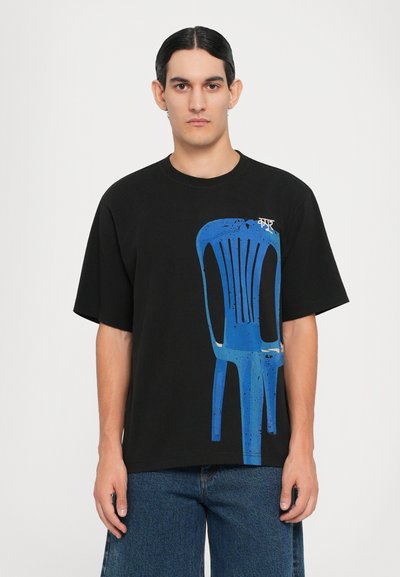 T-shirt en coton noir avec un motif d'une chaise bleue, des lignes audacieuses et une coupe décontractée. Le design comprend des détails de éclaboussures et des manches courtes.