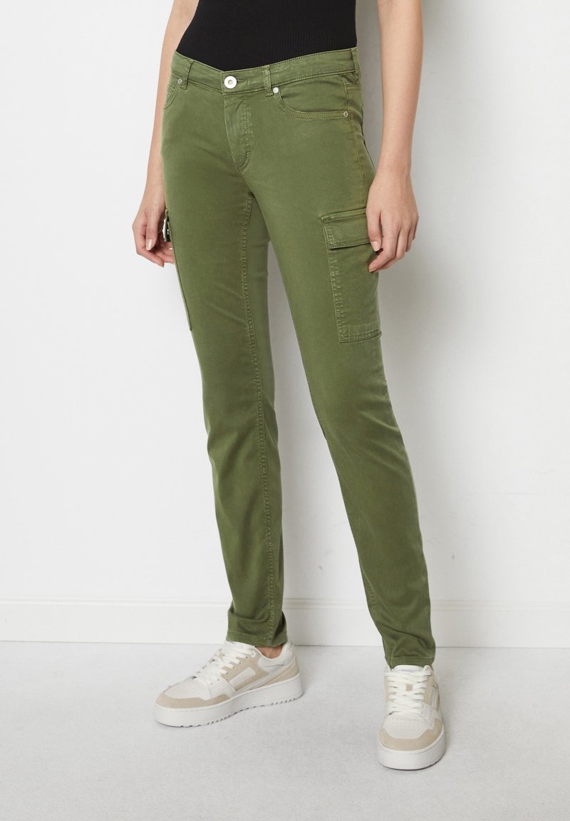Pantalon cargo slim fit vert olive avec poches latérales porté avec des baskets blanches et beiges et un haut noir.