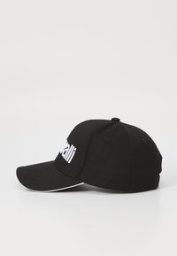 Svart baseball caps laget av bomull med buet skygge. Har hvit brodert tekst på fronten og hvite detaljer langs kanten av skyggen.