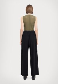 Top sans manches vert olive avec un col haut, associé à un pantalon large noir avec des poches latérales et une taille élastique.