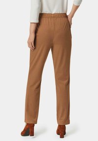 Pantalons marron à taille élastique avec une coupe droite, fabriqués en tissu doux. Associés à des chaussures à talons blocs rouges texturées.