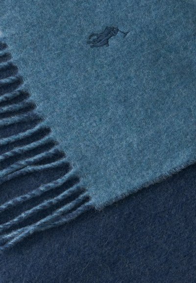 Écharpe en laine bleue douce avec bords frangés et petit logo brodé d’un cheval et d’un cavalier.
