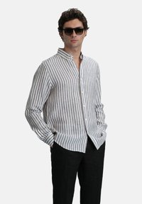 Gestreept, button-up shirt van lichtbeige en grijs stof. Bevat een kraag, lange mouwen en heeft een ontspannen pasvorm. Gdragend met zwarte broek.