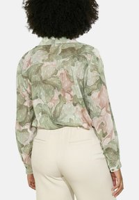 Long-sleeve shirt featuring a sheer, floral fabric in green and pink with a textured finish and polka dot accents. Back view shown.
