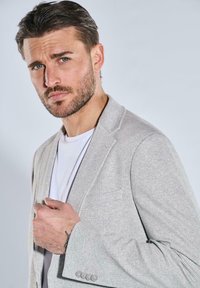 Light grey, striped blazer with a notch lapel and a single chest pocket, worn over a white t-shirt. Features a tailored fit and subtle texture.