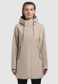 Veste imperméable beige avec capuche, fermeture éclair à l'avant et accents de fermeture éclair noirs. Présente des manches longues et des poches latérales. Texture lisse.