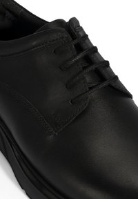 Zwarte leren schoen met een gladde textuur, ronde neus en een klassieke vetersluitingen met vier veterogen en subtiele stikseldetails.