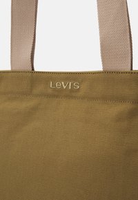 Torba płócienna w musztardowym kolorze z jasnobrązowymi uchwytami. Wyposażona w logo wyhaftowane oraz teksturowaną powierzchnię. Trwała i przestronna konstrukcja.