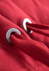 Rode stof met een gestructureerd oppervlak, voorzien van zilveren metalen oogjes en bijpassende koord, die een snug en functioneel ontwerp tonen.