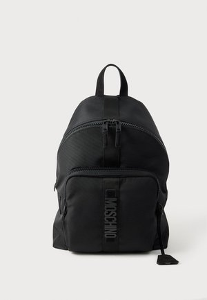 Czarny plecak Moschino z górnym uchwytem, przednią kieszenią na zamek błyskawiczny oraz widocznym logo na pasku przedniej kieszeni na jednolitym jasnym tle.