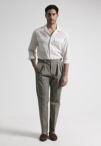 Camisa blanca de botón con dos bolsillos en el pecho, combinada con pantalones de corte recto en gris claro y zapatos de ante marrón. Diseño simple y ajustado.