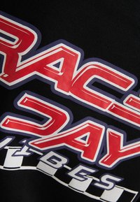 Tučné červené a bílé stylizované písmo "RACE DAY" na černé látce s bílým a černým kostkovaným vzorem a menšími písmeny níže.