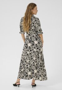 Robe maxi à motifs floraux noir et blanc avec des manches longues, des détails froncés et une taille cintrée. Stylisée avec des sandales à talons noires.