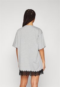 Szara, oversize sukienka t-shirta z krótkimi rękawami i czarną koronką na dolnym brzegu, charakteryzująca się miękką fakturą i luźnym krojem.