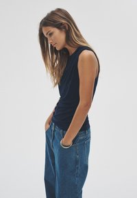 Navy sleeveless top with gathered fabric details, paired with high-waisted blue denim jeans. The jeans have a relaxed fit and side pockets.
