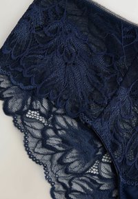 Marineblaue Spitzenunterwäsche mit floralen Mustern, gewellten Rändern und transparenter Textur, die komplexe Details und ein zartes Design präsentiert.