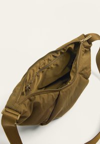 Borsa a tracolla khaki realizzata in morbido tessuto con chiusura a zip. L'interno presenta una fodera liscia e una piccola tasca con zip per una migliore organizzazione.