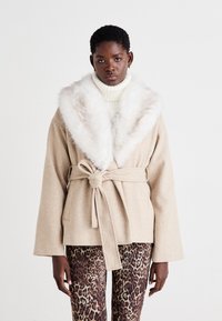 Šviesiai ruda apsiaustė su dideliu dirbtiniu kailiu, surišta ties juosmeniu. Ilgos rankovės ir minkšta tekstūra. Dėvima ant leopardų rašto kelnių.