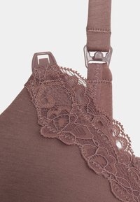 Rjav čipkast modrček, ki ima teksturirano mat tkanino, zapleten čipkast rob vzdolž zgornjega roba, nastavljive naramnice in plastične dodatke.