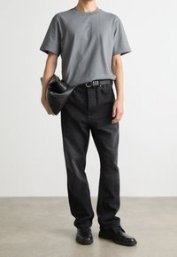 Grijze katoenen T-shirt, losse zwarte jeans, zwarte leren clutch en zwarte schoenen. Eenvoudig ontwerp met een neutraal kleurenpalet.