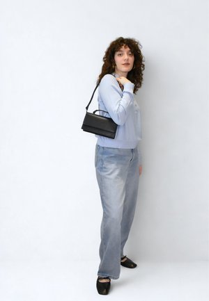 Czarna skórzana torba na ramię, o prostokątnym kształcie, minimalistyczny design, noszona z jasnoniebieską bluzką z długim rękawem i jasnymi dżinsami.