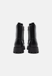 Bottines en cuir noir avec une semelle épaisse, des fermetures éclair à l'arrière et des tirettes ; design élégant avec une texture lisse et une finition durable.