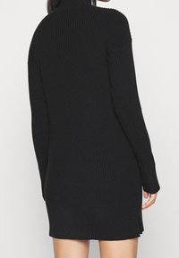 Abito in maglia nera a coste con colletto alto, maniche lunghe e spacchi laterali all'orlo, caratterizzato da un design testurizzato e aderente.
