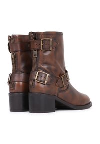 Botas de tobillo de cuero marrón con un acabado desgastado, que cuentan con dos correas decorativas con hebillas de metal, cremalleras laterales y un bajo tacón cuadrado.