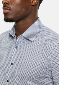 Hemd mit Knopfleiste in Hellblau mit einem geometrischen Muster in Marineblau. Verfügt über einen klassischen Kragen und blaue Knöpfe, glatte Stofftextur.