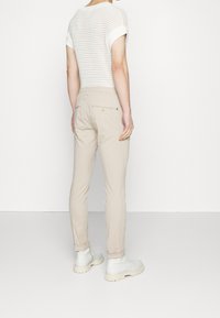 Pantalon beige fuselé à texture lisse, doté de poches arrière et d'un détail à fermeture éclair, associé à un haut en maille légère blanc.