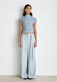 Blue crop top with a high neck and cap sleeves paired with light blue wide-legged trousers, featuring a belt and pleats.