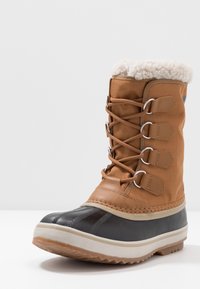Botas de invierno de tela marrón y cuero con un collar forrado de felpa, caperuza de goma en la punta, media suela blanca en cuña y detalles texturizados en gris.