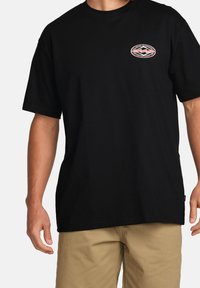 Sort bomulds t-shirt med korte ærmer, rund hals og et lille cirkulært logo i rød og hvid på venstre bryst.