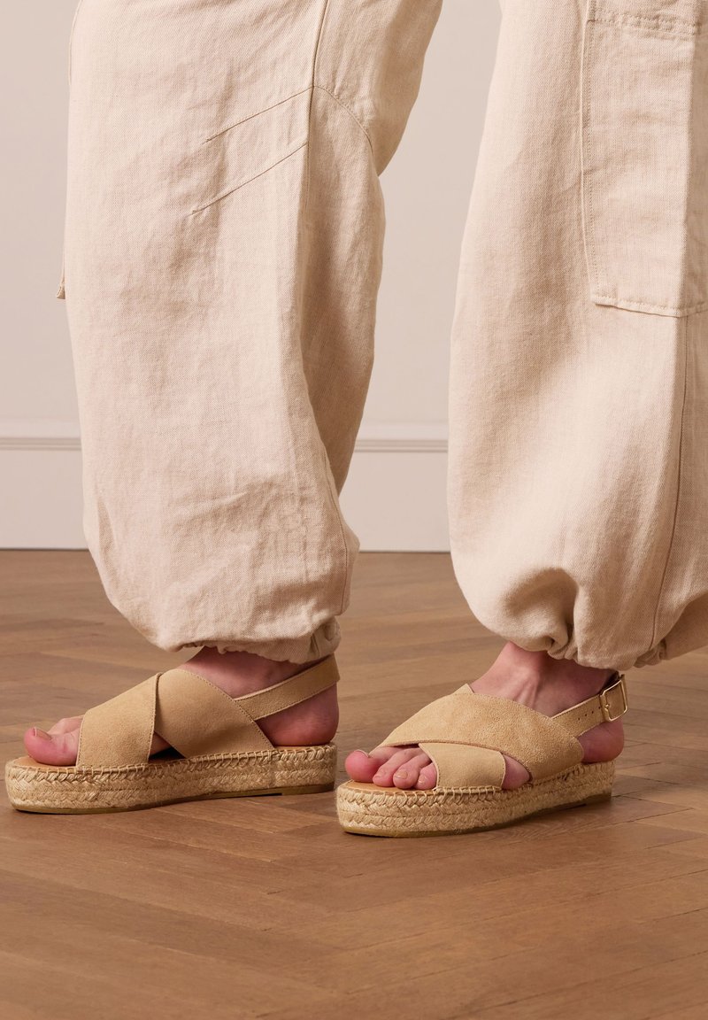 Beige suede espadrille sandalen met kruislingse banden en een jute-wikkelzool. Gemaakt in combinatie met losse beige stoffen broek.