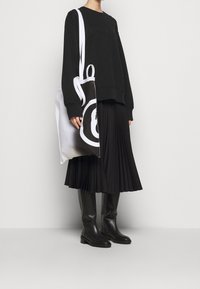 Černá mikina, plisovaná černá sukně, černé vysoké boty až po kolena a velká taška s bílým a černým kruhovým designem.