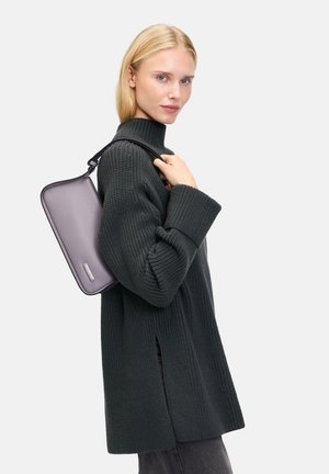 Grauer Strickpullover mit langen Ärmeln; das Modell hält eine lavendelfarbene Tasche mit Reißverschluss, die ein kleines metallisches Akzent hat. Schlichte, strukturierte Form.