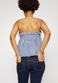Top peplum às riscas azuis e brancas com babados, alças finas ajustáveis e uma silhueta evasê. Usado com jeans azul escuro.