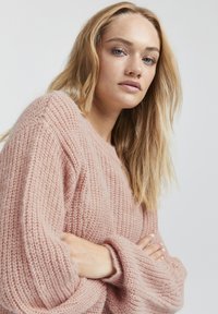 Maglione rosa chiaro lavorato a maglia con una vestibilità comoda, texture a coste e maniche larghe. Il tessuto appare morbido e leggero, con un design accogliente.