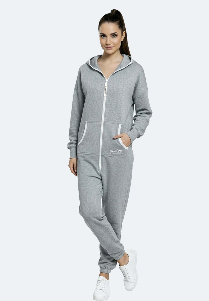 Salopette grigia con zip e cappuccio, due tasche frontali, polsini elasticizzati e dettagli bianchi. Realizzata in un tessuto morbido.