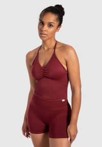 Bordeaux sportoutfit met een halternek crop top met plooidetail en hoge taille shorts, gemaakt van elastische stof.