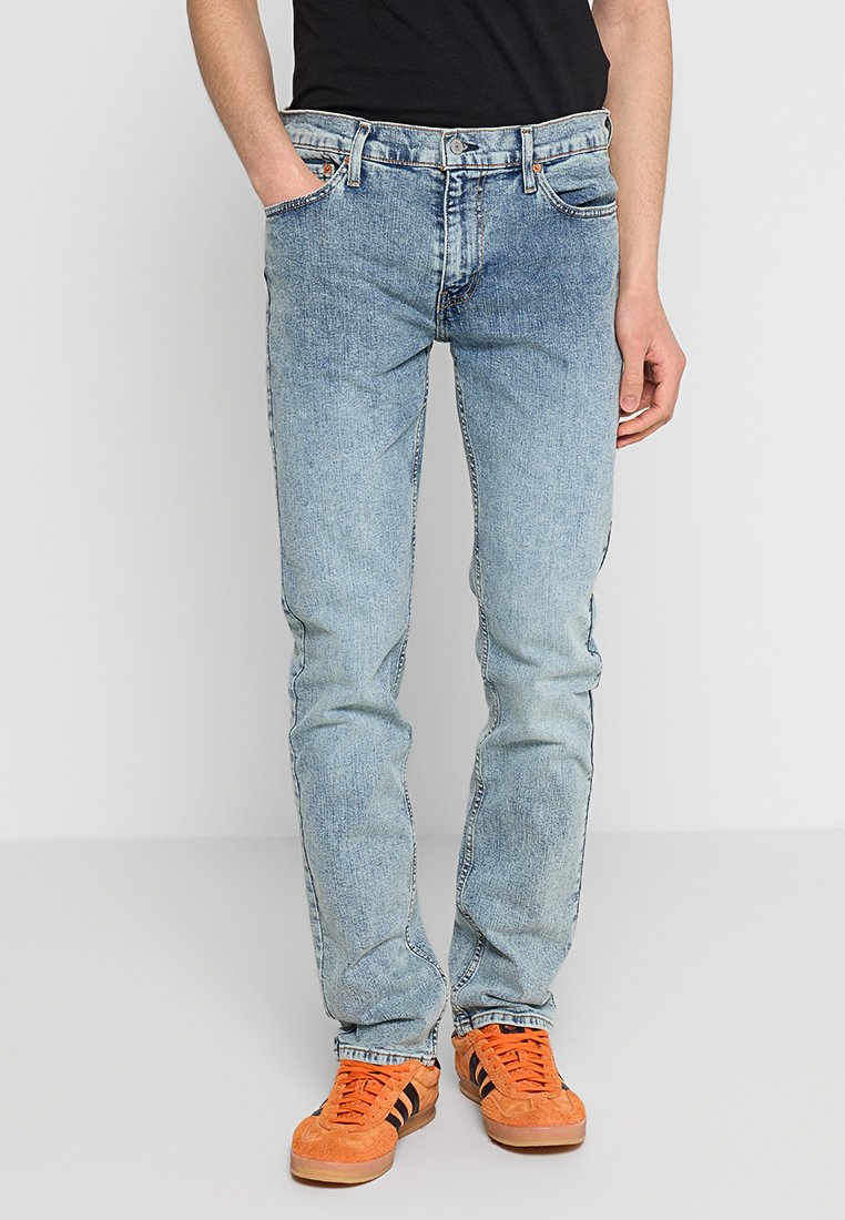 Jeans de mezclilla azul claro con corte slim, que cuentan con un diseño de cinco bolsillos y un ligero desgastado. Combinados con zapatillas naranjas.