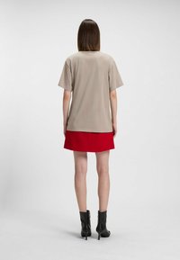 Haut à manches courtes beige clair associé à une jupe A-line rouge, porté avec des bottines noires. Texture lisse, design épuré, coupe mi-longue.