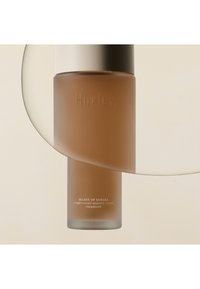 Huxley Conditioning Essence Toner, cilindrische glazen fles, mat amberkleur, zilveren dop, geperst logo, minimalistisch ontwerp, witte tekst aan de onderkant.