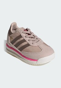 Svetloružová teniska z kombinácie zamatovej a sieťovinovej látky, hnedé pruhy, biela medzipodrážka a ružový akcent na podrážke. Klasický športový dizajn.