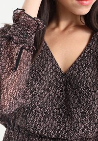 Vestido negro con pequeño estampado floral en rosa, con mangas transparentes y con volantes, además de un escote en V. Tela suave con un diseño fluido.
