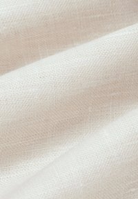 Biała tkanina lniana o delikatnym, teksturowanym splocie. Miękkie, naturalne włókna tworzą subtelną, nieco nieregularną strukturę powierzchni.