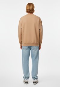Felpa beige con una vestibilità rilassata, polsini e orlo a costine; abbinata a jeans larghi azzurri e sneakers bianche.