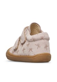 Světle růžová dětská bota s hnědou gumovou podrážkou, dvěma suchými zipy a malými vzory mašlí tištěnými na semišovém materiálu.