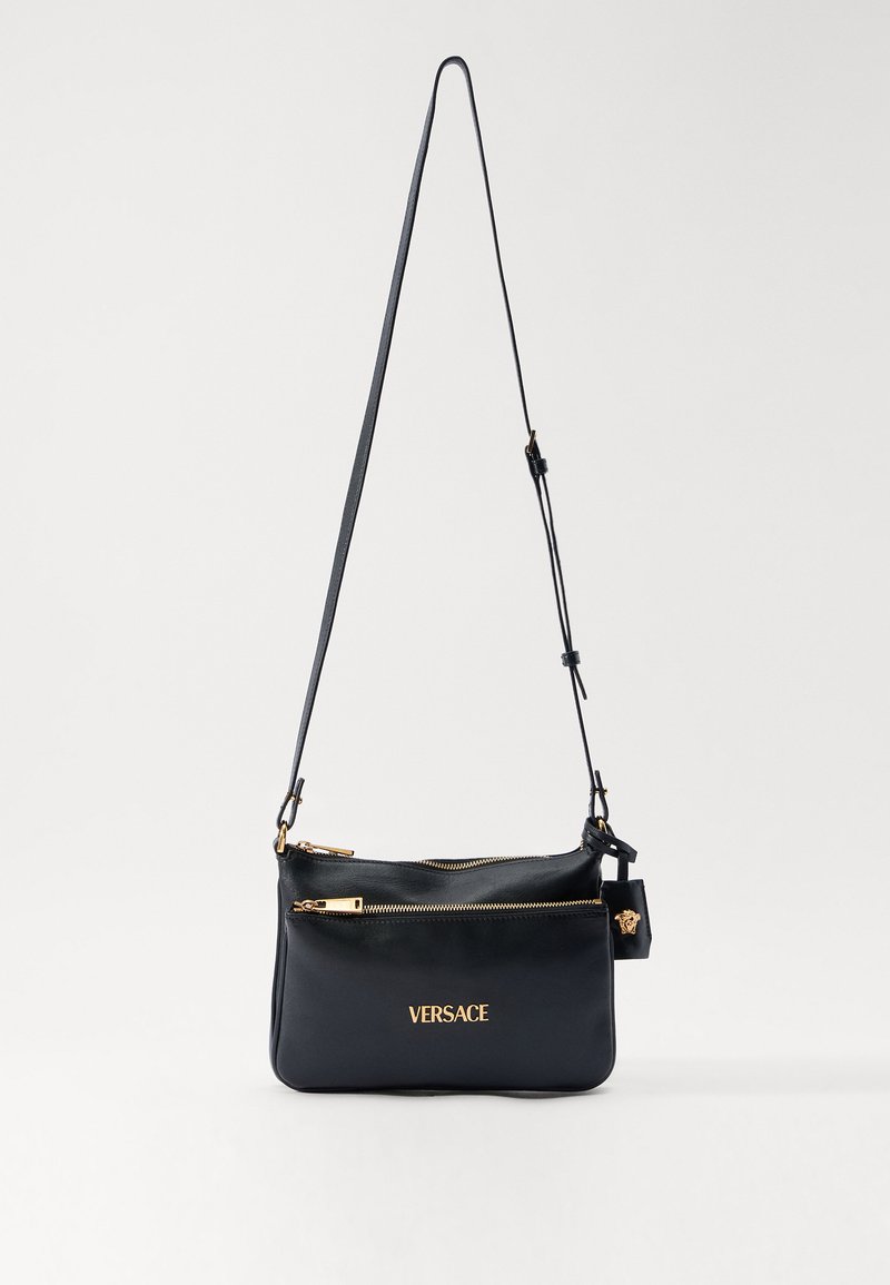 Black leather crossbody bag with adjustable strap, gold zippers, and gold "VERSACE" logo on front pocket.