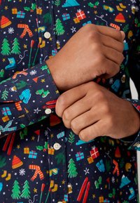 Camicia a maniche lunghe con sfondo blu navy scuro, caratterizzata da stampe colorate a tema festivo come alberi, regali e accessori invernali.